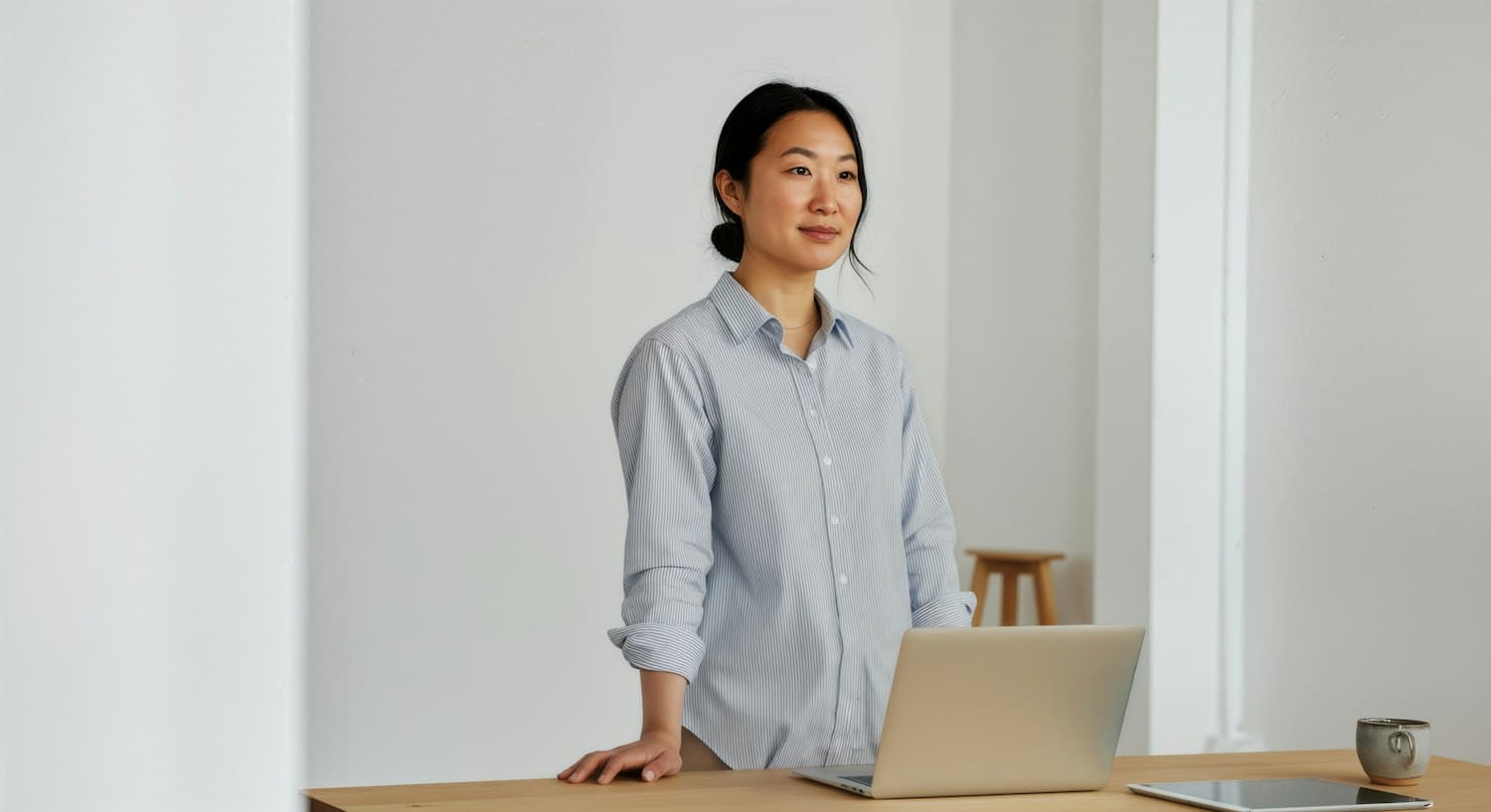 A person standing at a desk with a laptop in a bright, quiet room